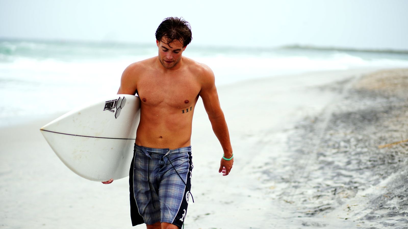 Surfer walking up the beach carrying a white shortboard