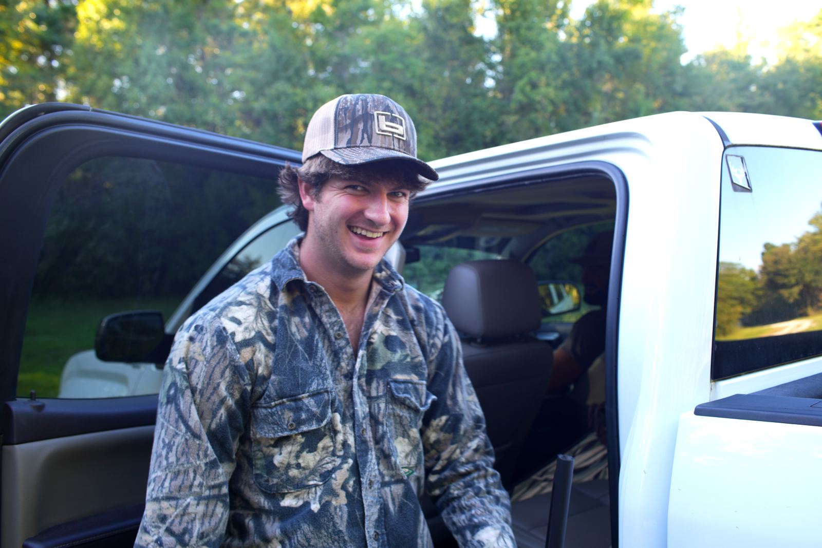 Tanner in camouflage smiling beside the open door of a white truck