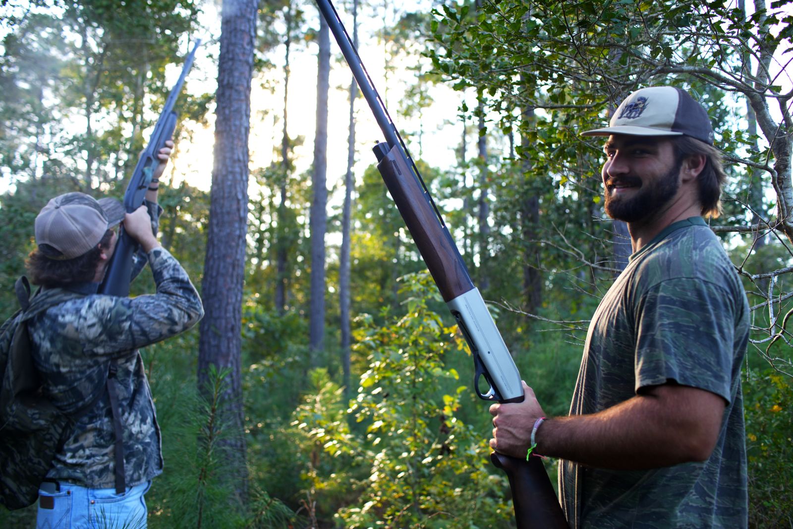 Tanner and Turner looking up into tall pines, shotguns raised