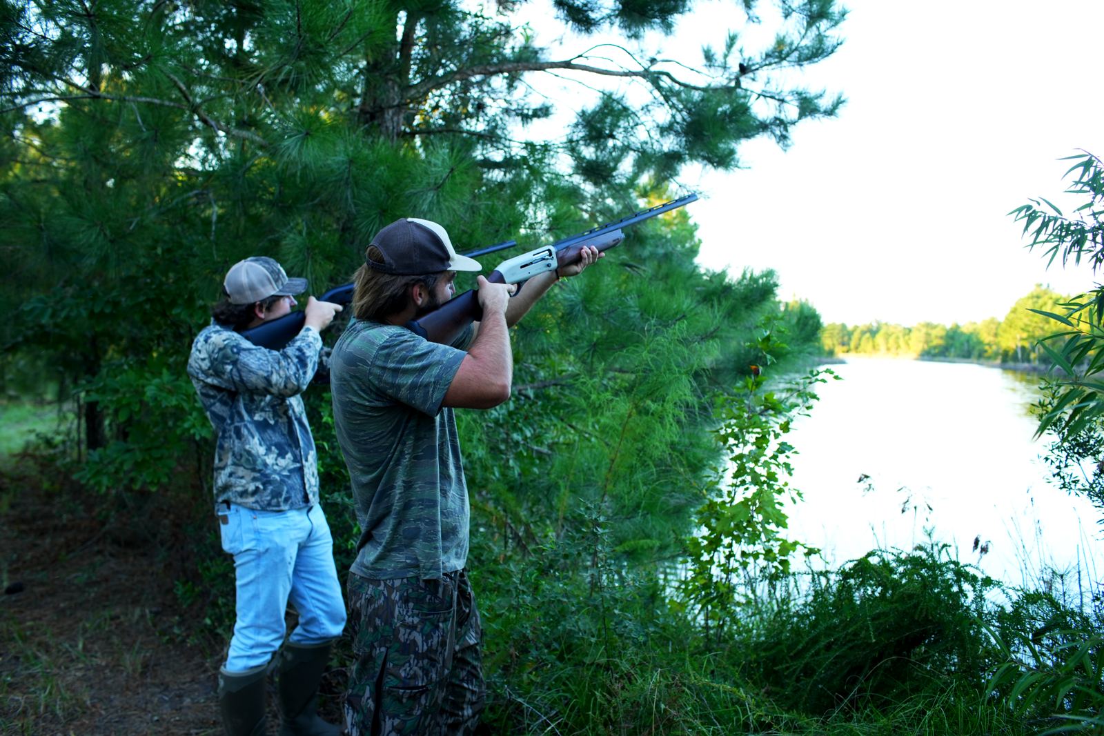 Tanner and Turner shouldering shotguns at the edge of a lake