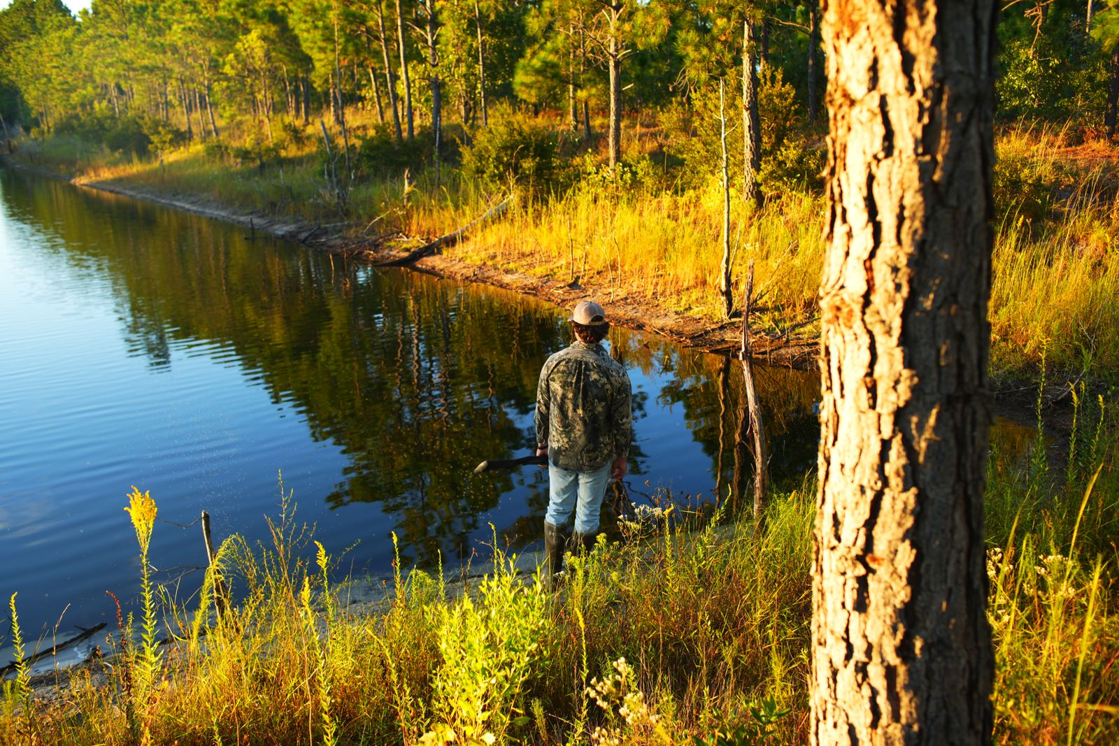 Tanner standing at the edge of a still lake in golden light