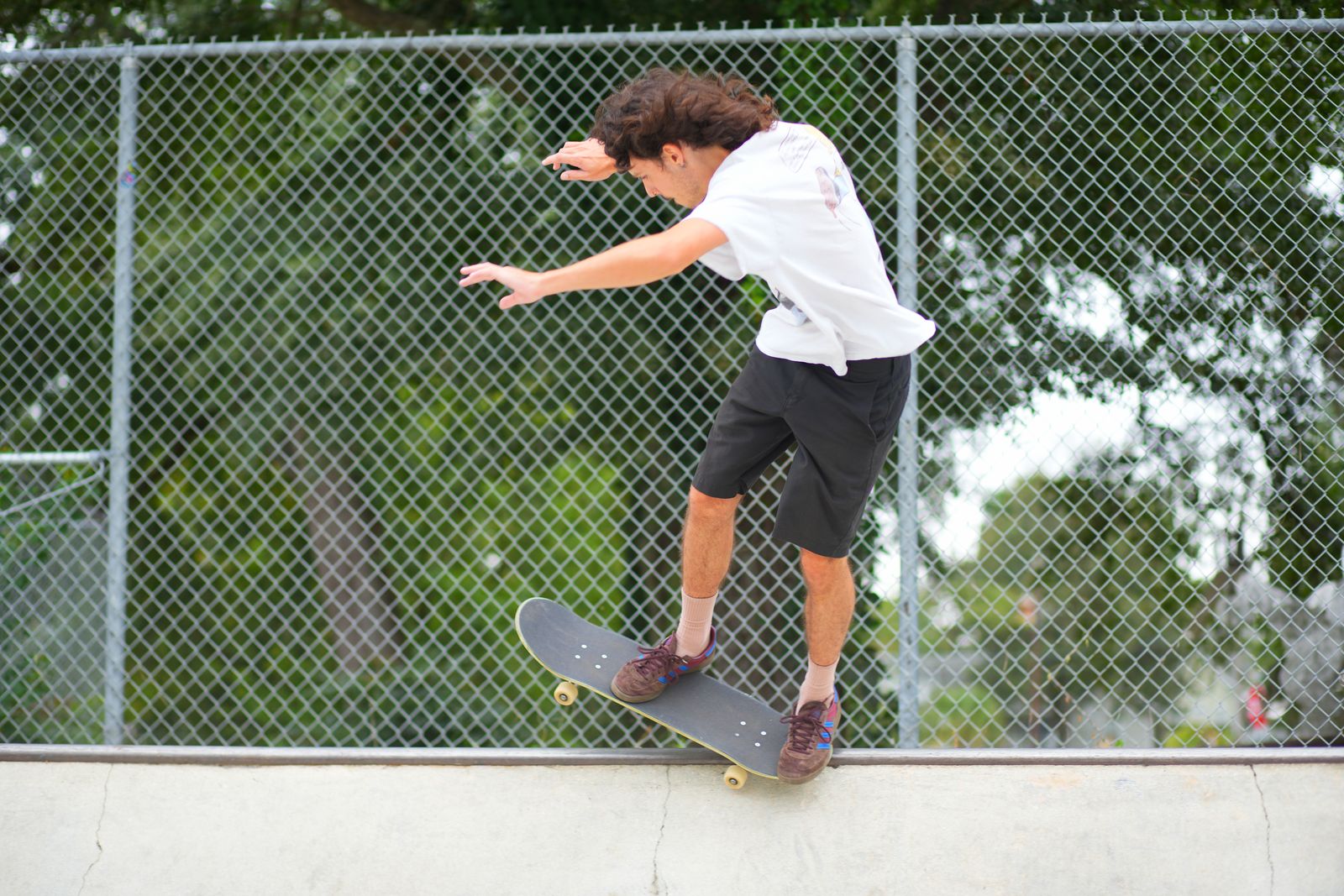 Jaden in a 5-0 along the coping with the chain-link fence behind