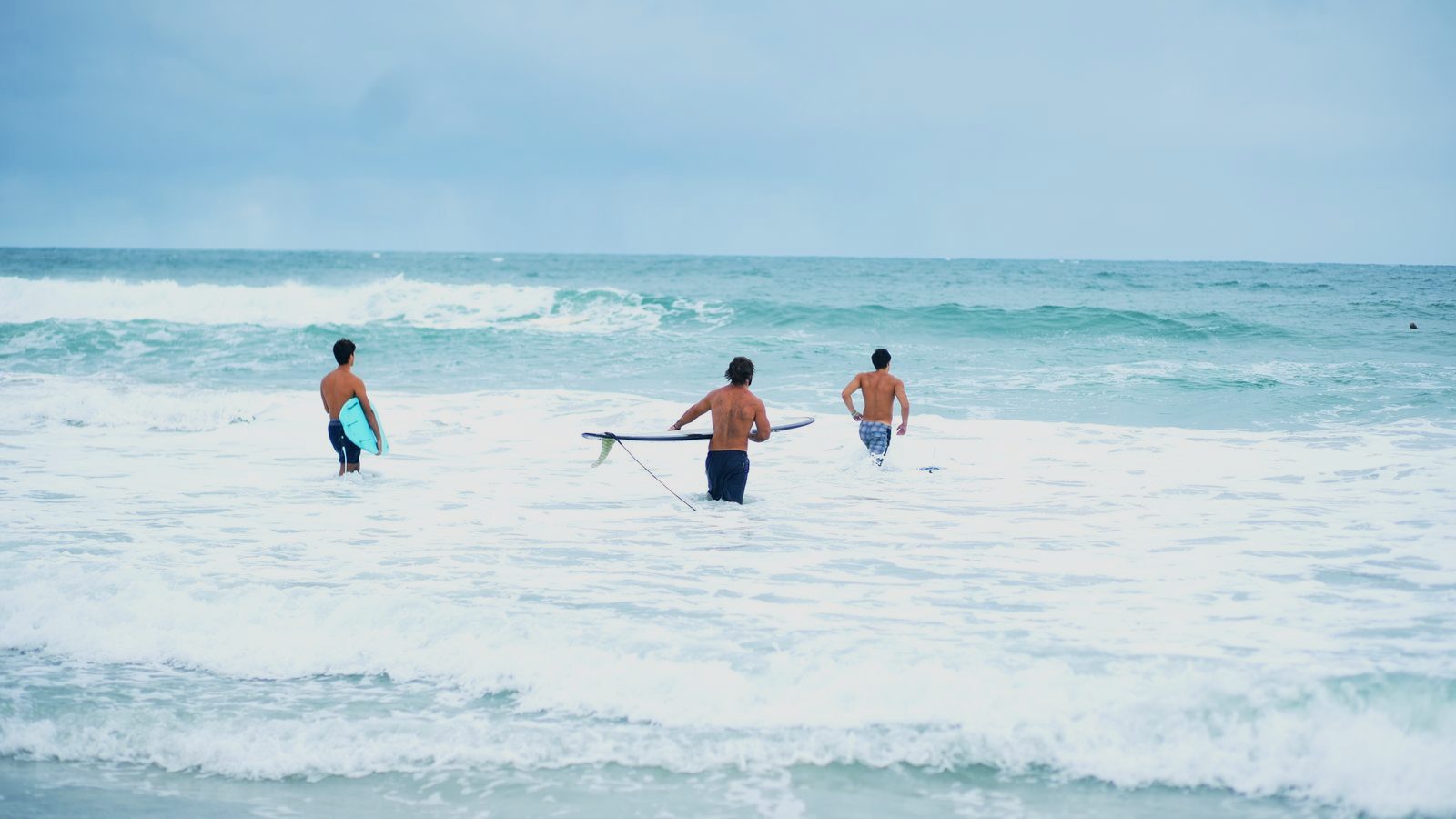 Three surfers wading out through the whitewater with their boards