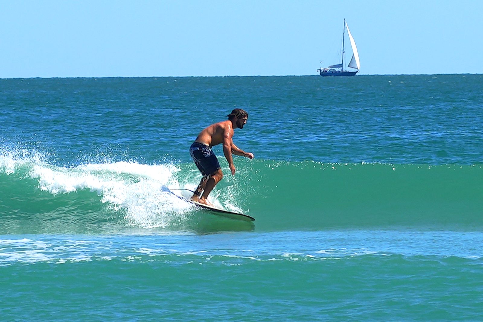 Turner trimming down the line on a clean green wave with a sailboat on the horizon